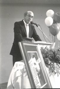 Stevens at a podium. Balloons and flowers on podium. 