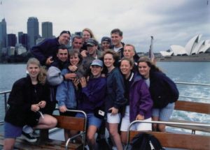 Students gather for a photograph on a boat. Sydney skyline, including the opera house, in background. 