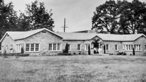 A one-story brick building with many windows and a grass lawn in front.