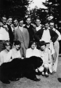 12 students pose with a large bear pelt, trees in background. 