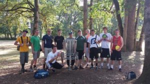 11 Disc golf club members at a disc golf club course, trees in background.  