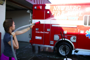 A young woman uses a hose to wash the Newberg Fire Department Medic Unit vehicle. 