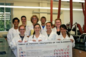 9 Sigma Zeta club members in lab coats pose for picture in a lab.  