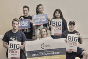 Turning Point USA group picture.  "Big Government Sucks," "Socialism Sucks," "Turning Point USA at George Fox University: Identity, Empower, Organize" signs.  