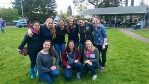 9 society of women engineers pose for a photo in a grassy field in a park.  